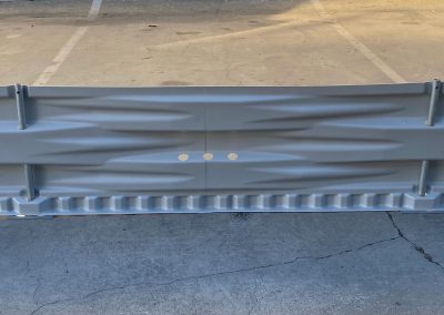 A large, gray metal guardrail with a textured pattern stands on a concrete parking lot.