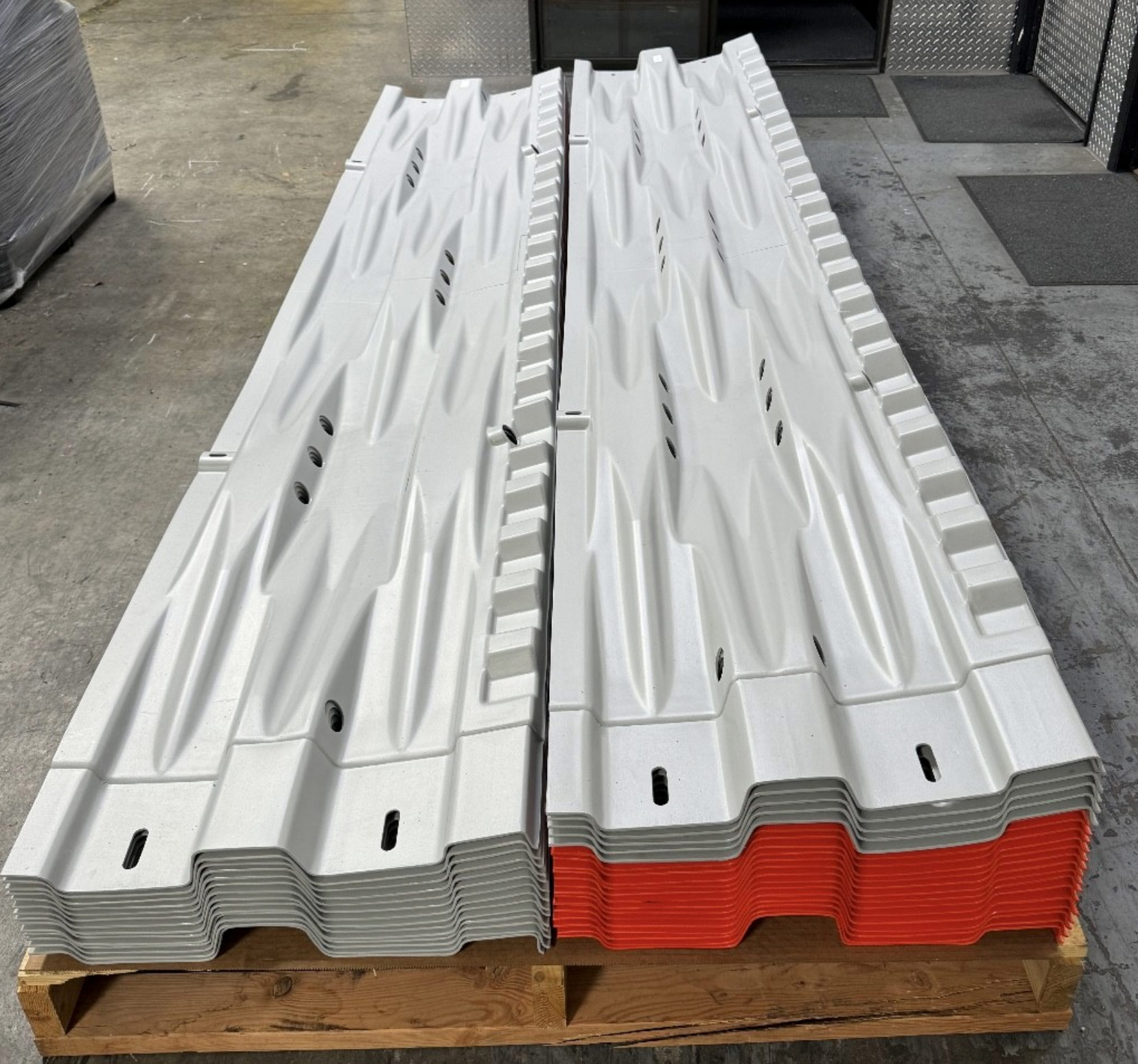 Stacks of gray and orange plastic panels with grooves, arranged on a wooden pallet in a warehouse.
