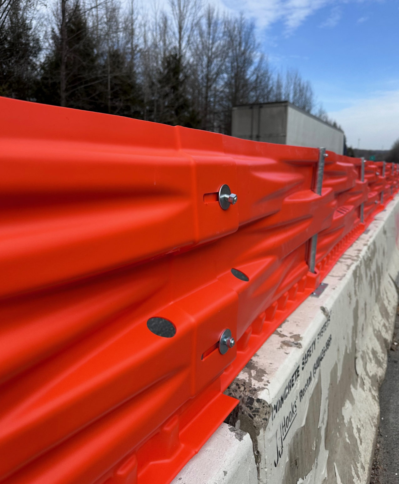 Close-up of bright orange highway guardrails attached to a concrete barrier, with trees in the background.