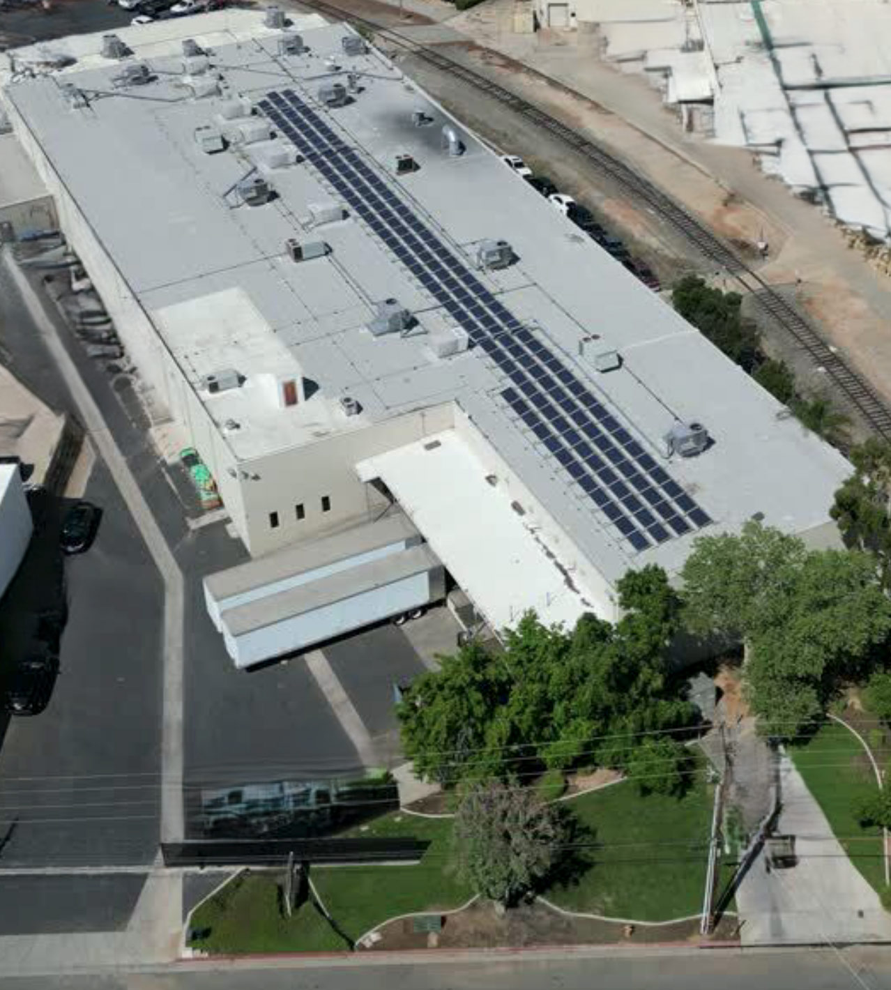 Aerial view of a large white building with solar panels on the roof and green trees surrounding it.