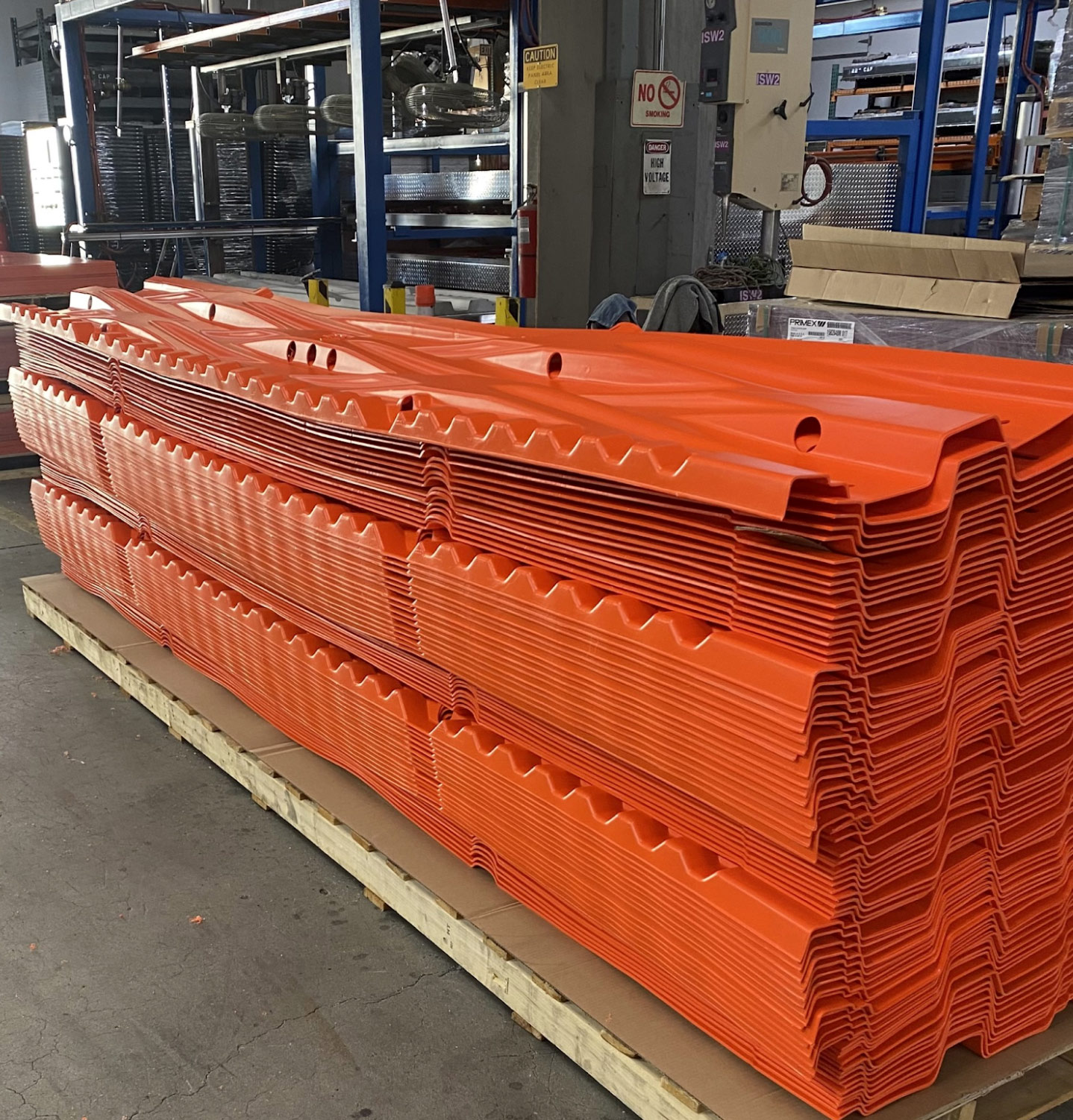 Stacks of bright orange plastic barriers are neatly arranged on a pallet inside an industrial warehouse by Beltway USA.