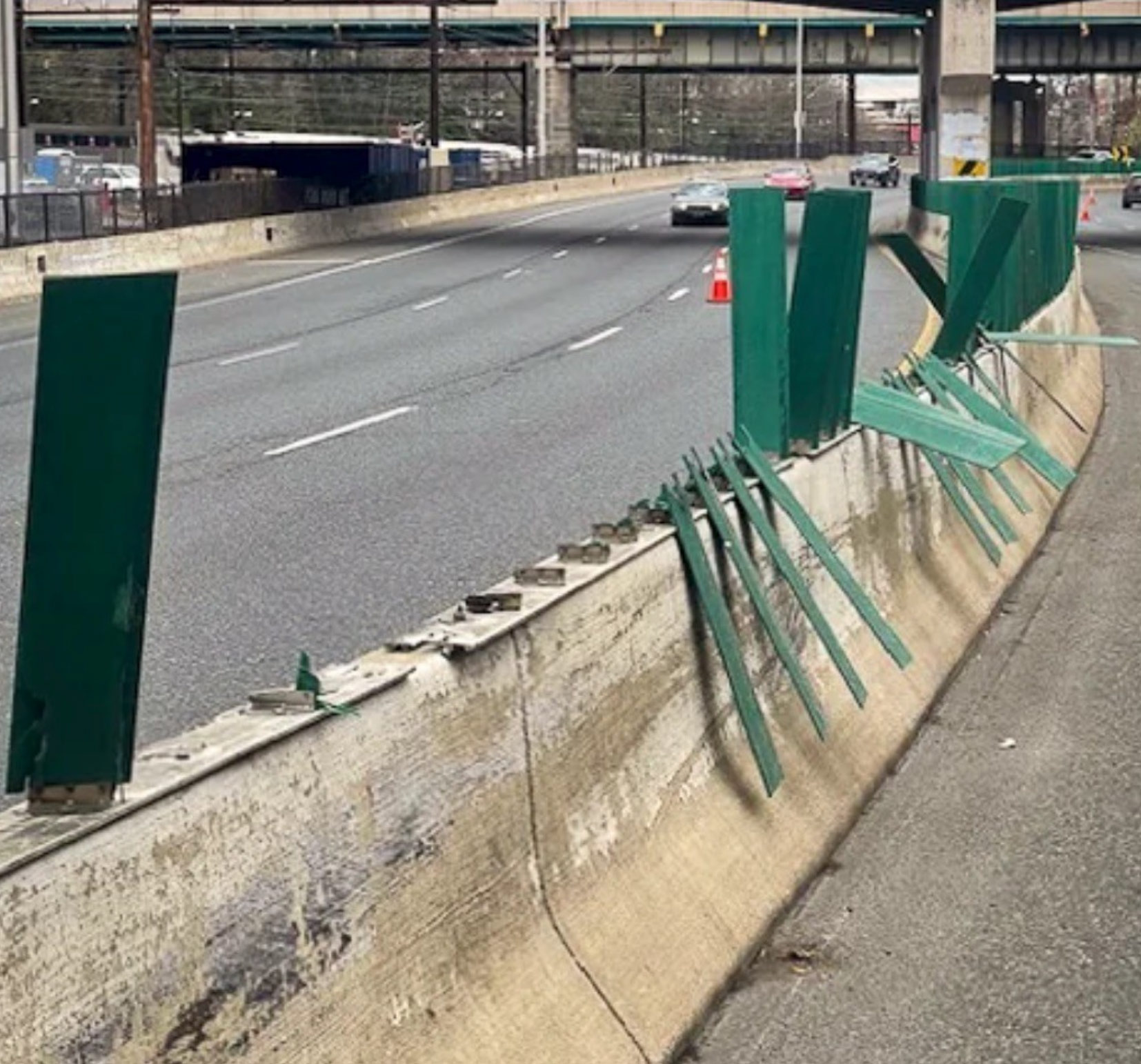 Green metal barriers on a highway divider are bent and damaged near moving traffic.