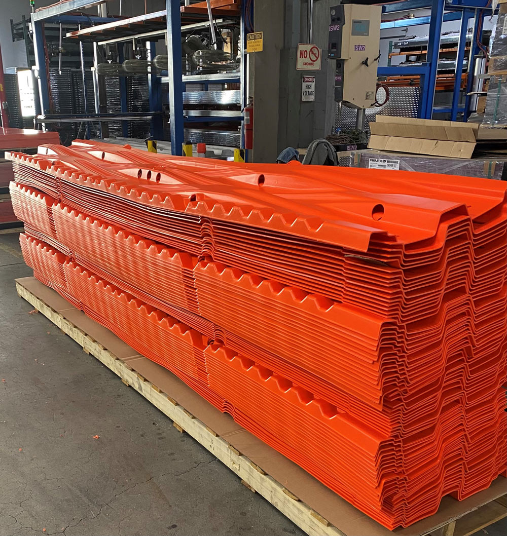 Stacked orange plastic sheets with wave patterns on a warehouse pallet, surrounded by industrial shelves.