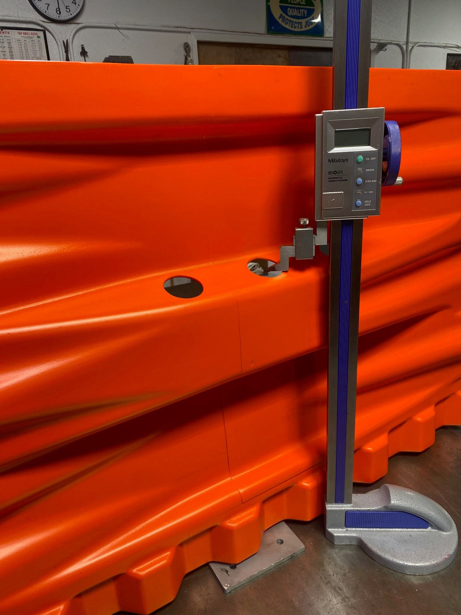 Height gauge measuring holes in a bright orange, corrugated plastic barrier on a workbench.