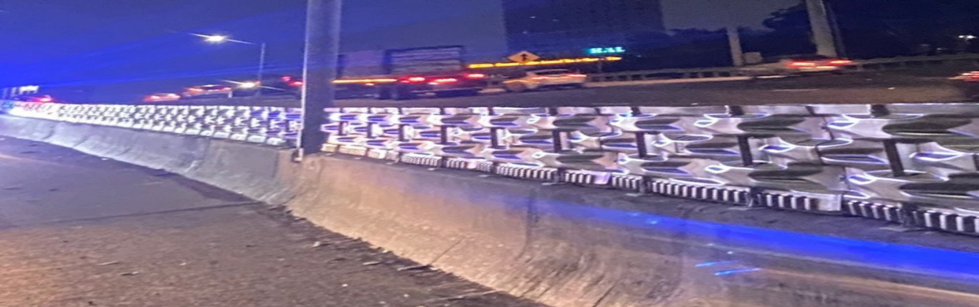 A highway at night with car lights and a decorative patterned barrier illuminated by blue lights.