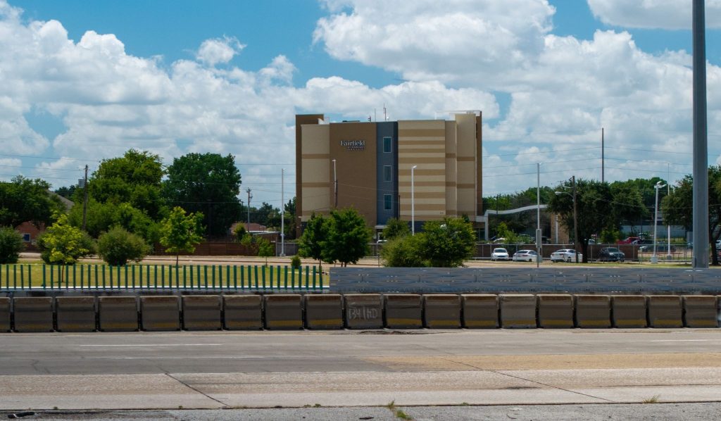 Hotel building in the background with trees and a road in the foreground under a partly cloudy sky.